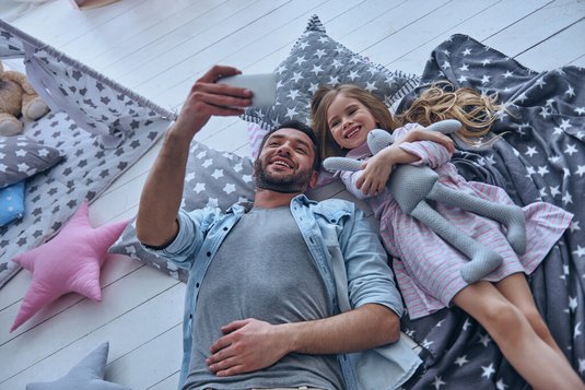 Vater und Tochter liegen auf dem Boden und machen Selfies